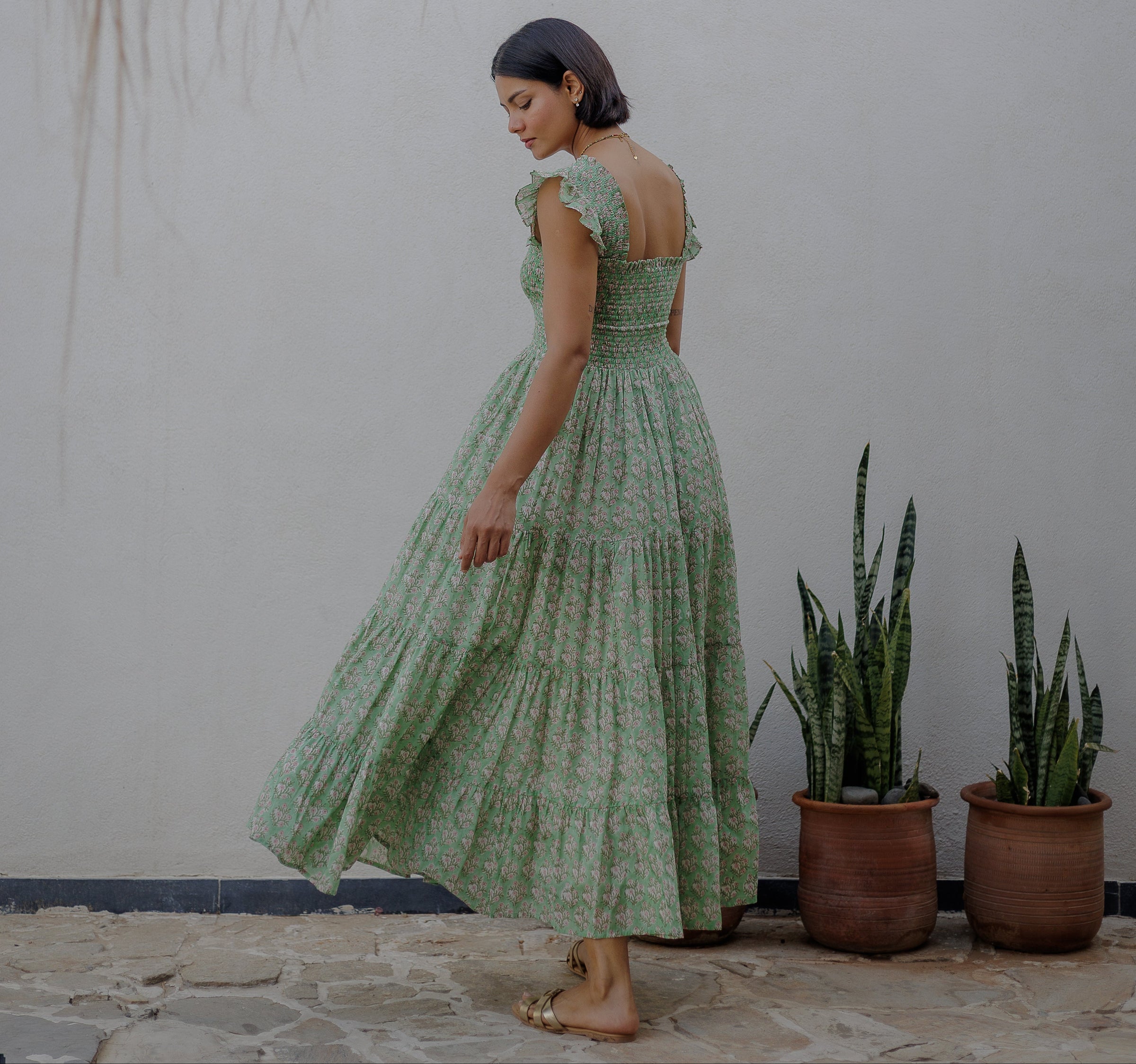 Woman in a green Tara dress, by Dilli Grey, standing in front of a white wall with potted plants.